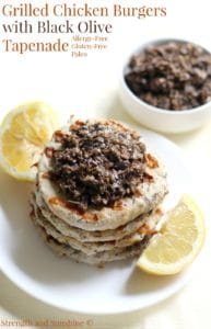 Grilled chicken burgers topped with black olive tapenade on a plate with lemons