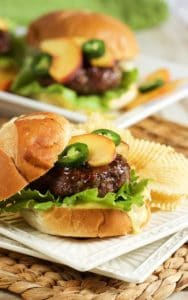 Hamburger topped with peaches and jalapenos alongside chips on a plate