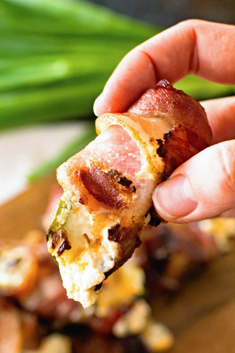 Hand holding grilled bacon wrapped jalapeno popper with cream cheese filling