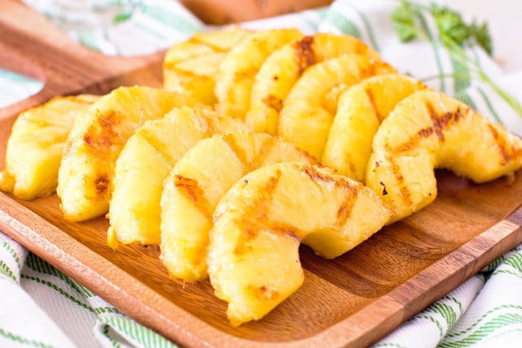 Pineapple slices with charred marks from grilling on wood platter