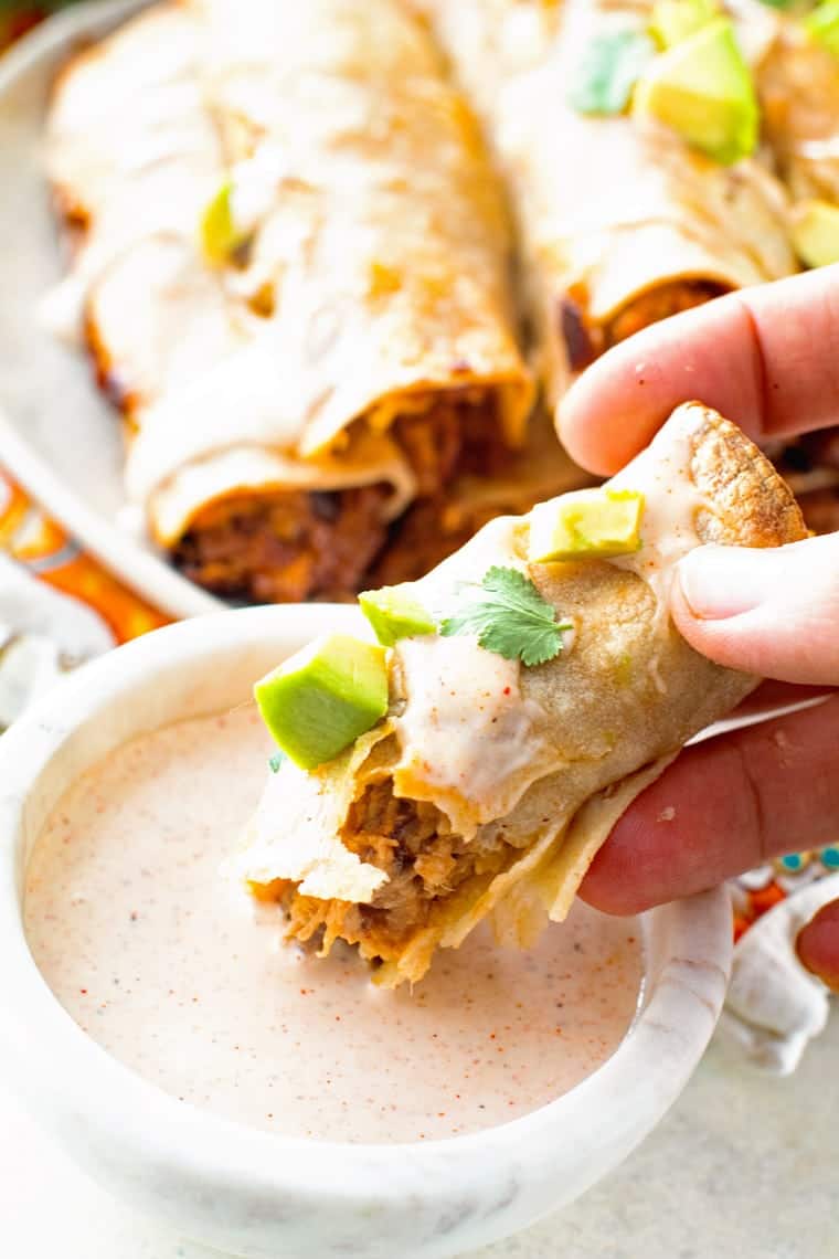 Hand holding taquito and dipping it into a Chiptole Ranch Dressing in a bowl