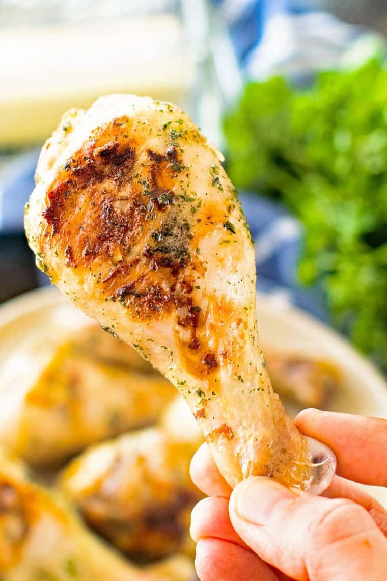 Hand holding grilled chicken leg with plate of chicken legs in background