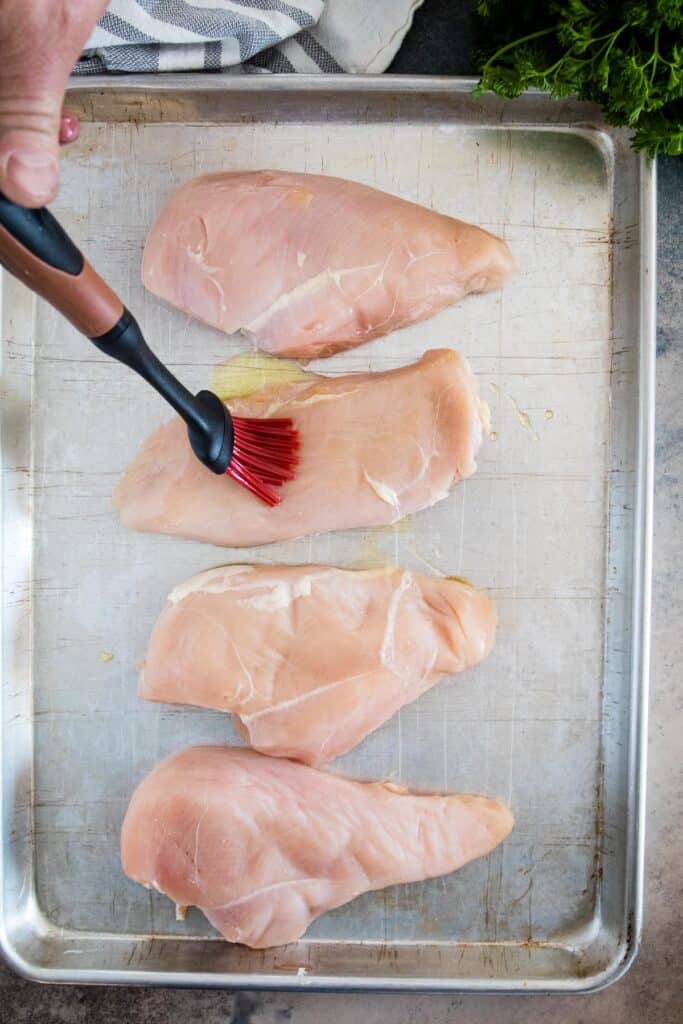 Basting brush putting olive oil on chicken breast