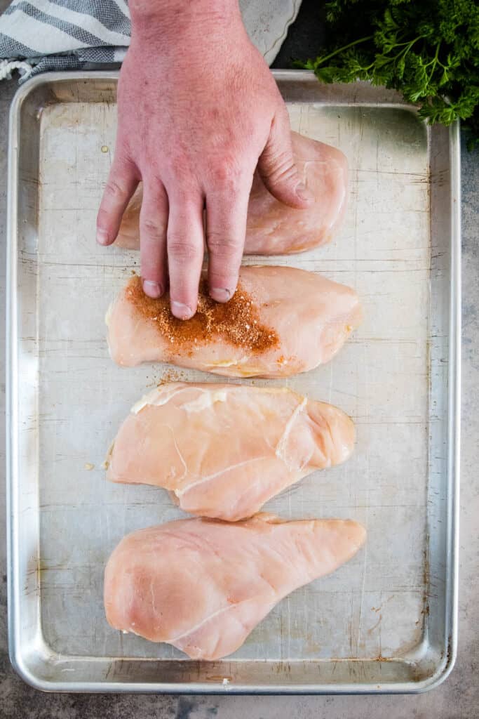 Hand putting seasoning on chicken breast