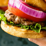 Hamburger topped with onion, tomato, and lettuce in hand