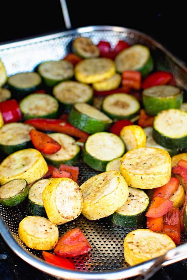 Grill pan with a mixture of green and yellow zucchini and peppers plus seasonings on a smoker
