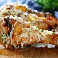 Three garlic parmesan chicken drumsticks on a wooden platter perfectly cooked! If you're hungry these are ready to be devoured!