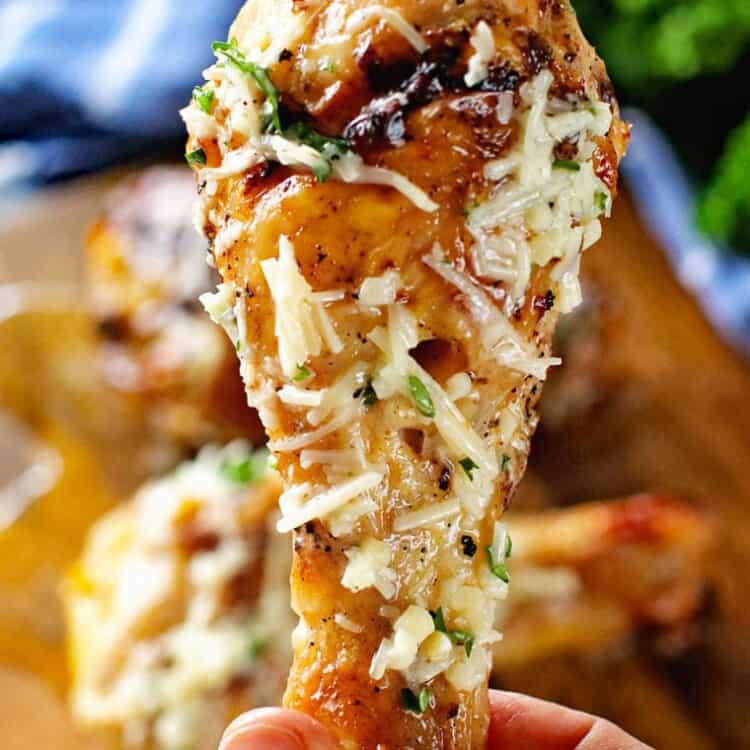 A platter of Garlic Parmesan Chicken Legs, with a close-up view of one of the grilled chicken legs coated in garlic parmesan .