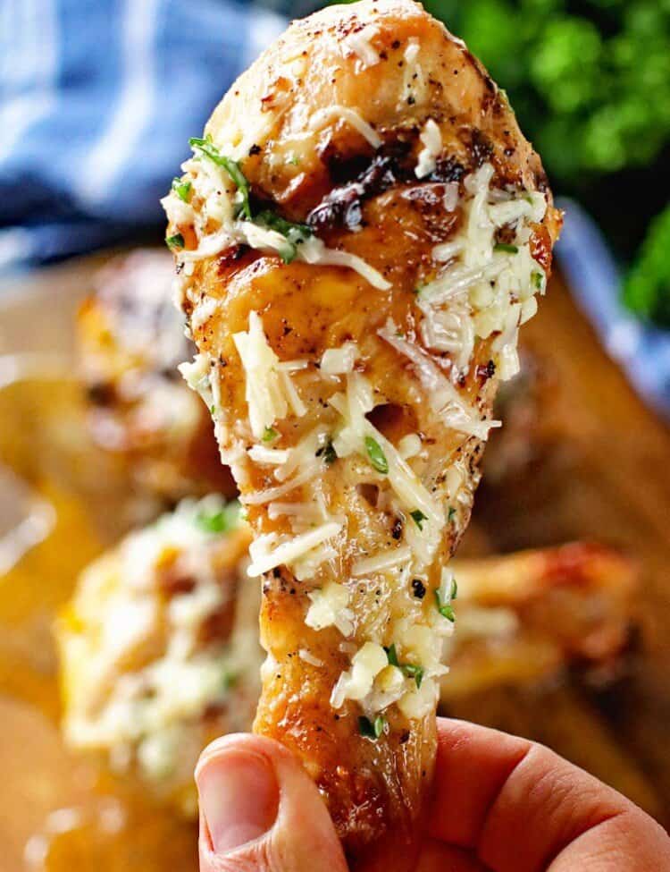 A platter of Garlic Parmesan Chicken Legs, with a close-up view of one of the grilled chicken legs coated in garlic parmesan .