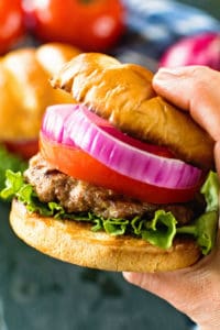 Hand holding best hamburger topped with lettuce, tomato, and onion.