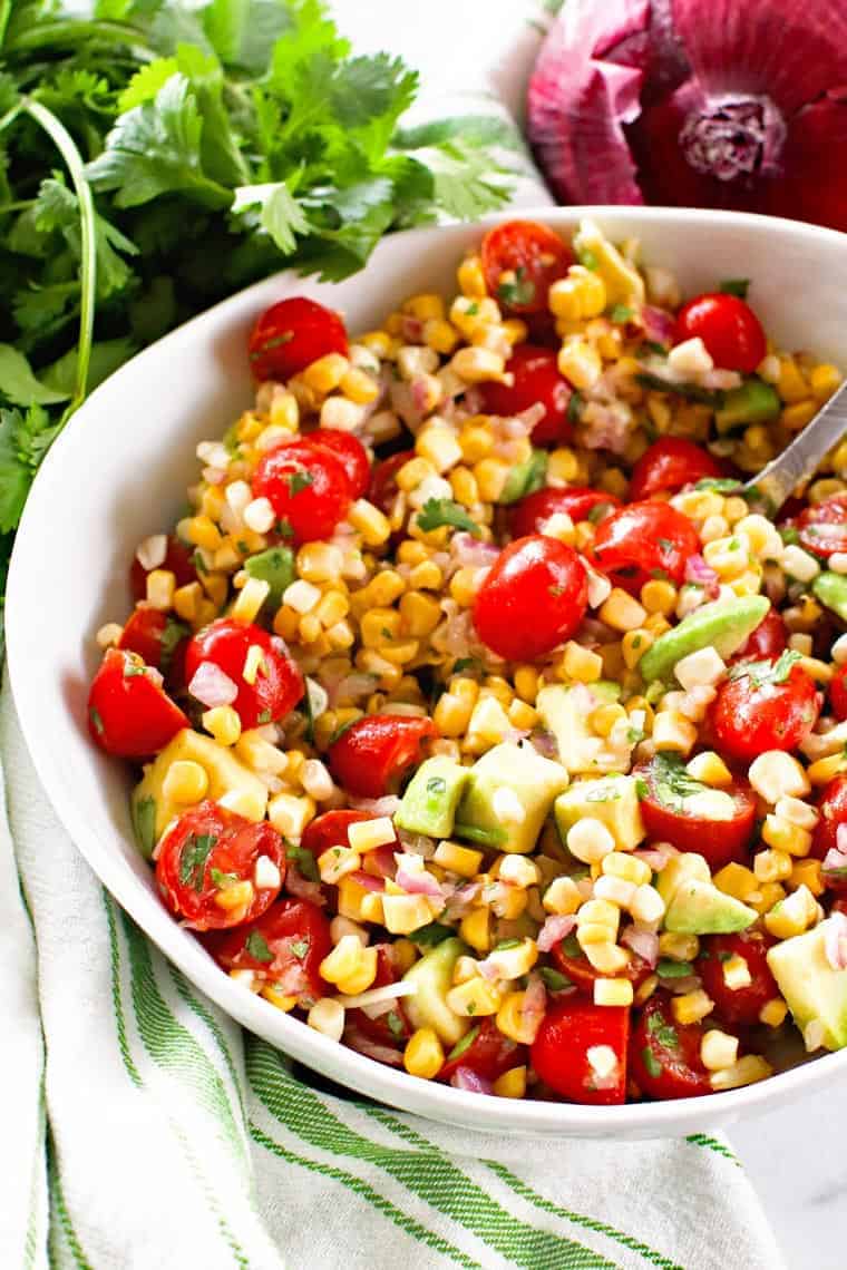 Corn Salad in white bowl with cilantro and red onion behind it