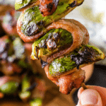 Hand holding grilled bacon Brussels Sprouts Skewer