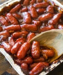 A pan of little smokies in bbq sauce with wooden spoon
