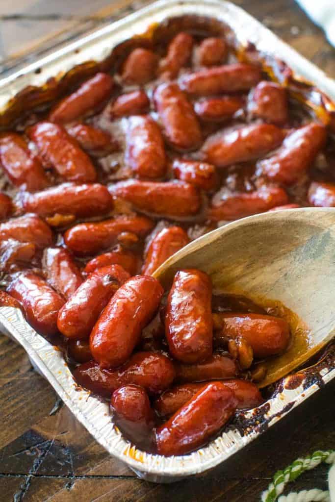 A pan of little smokies in bbq sauce with wooden spoon