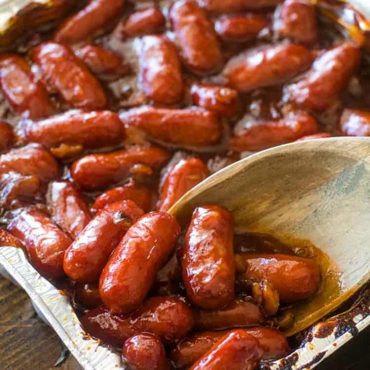 A pan of little smokies in bbq sauce with wooden spoon