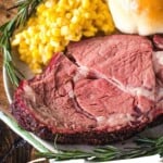 Smoked Prime Rib slice on a plate with corn and dinner roll