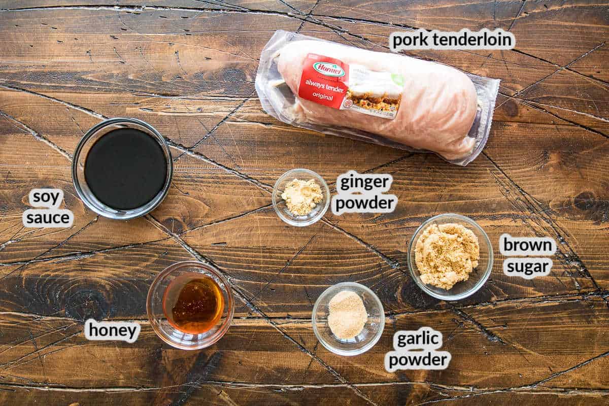 Overhead Image of ingredients on wooden board in glass bowls including soy sauce, honey, garlic powder, ginger powder, brown sugar and a pork tenderloin