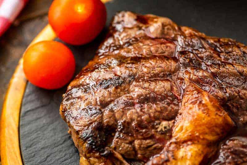 Juicy steak on slate cutting board with cherry tomatoes in the background
