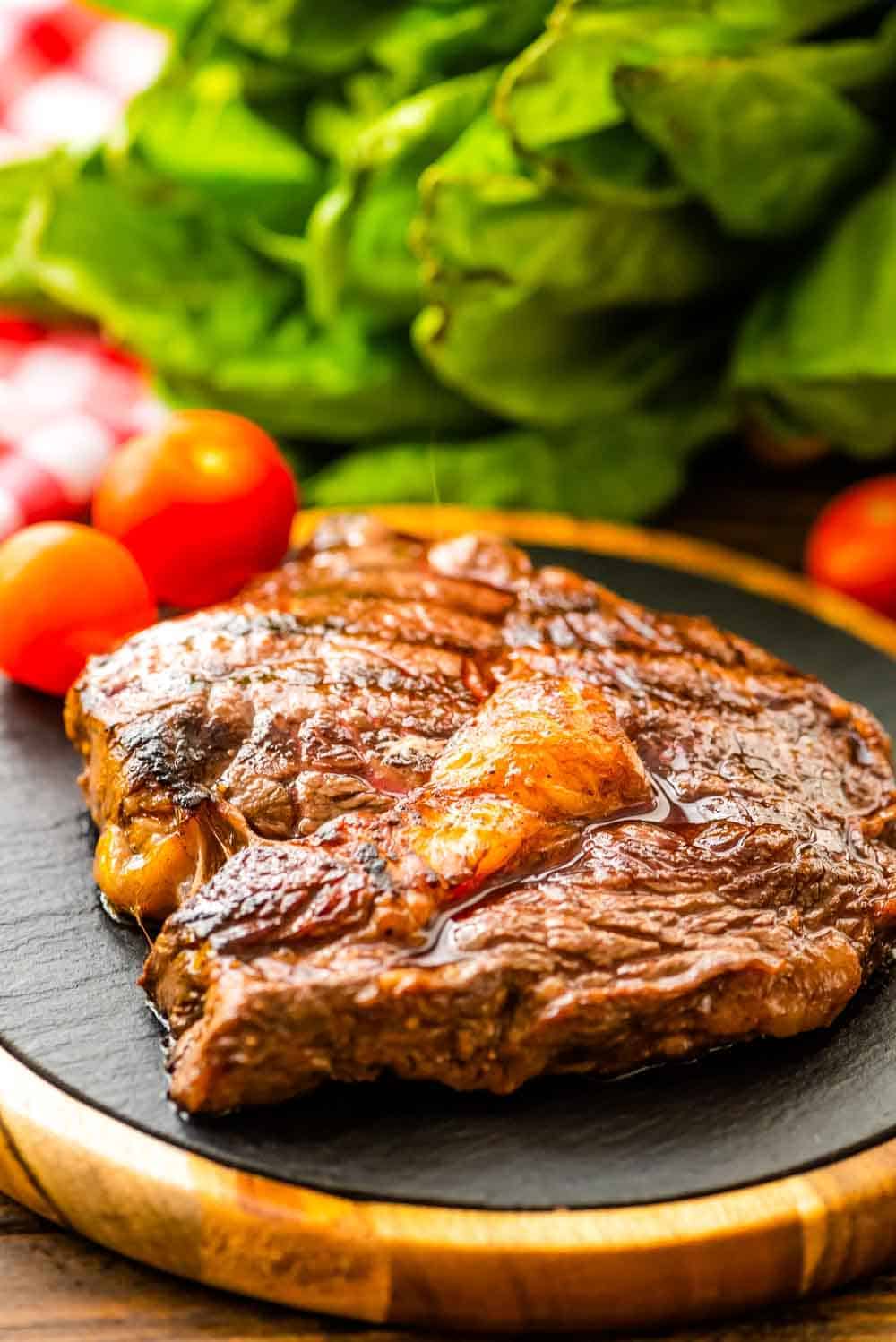 Red wine marinated steak on cutting board with cherry tomatoes and lettuce in background