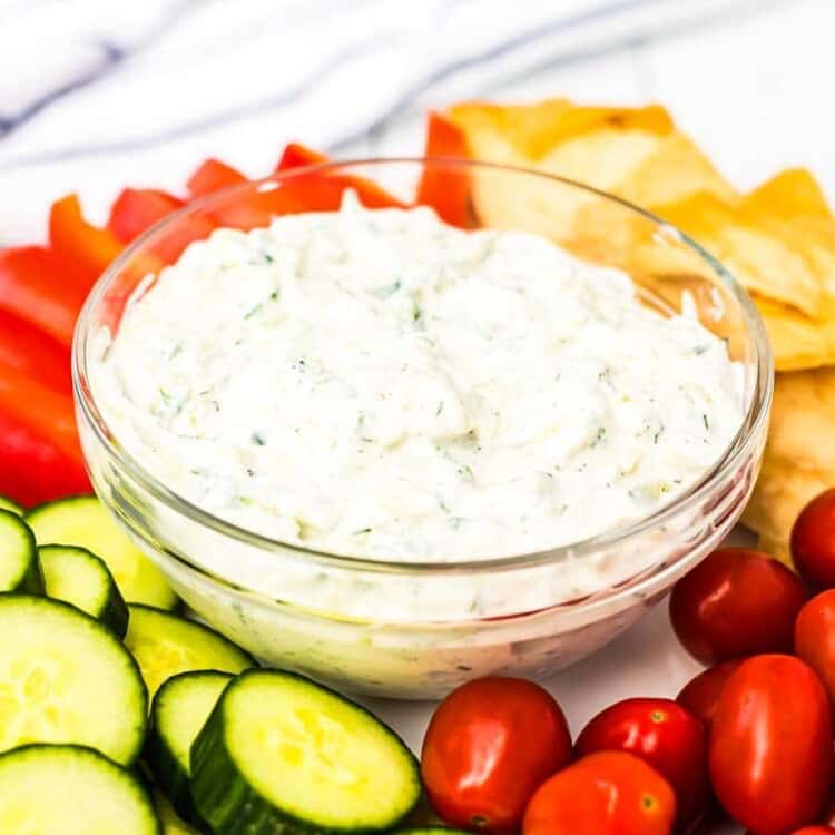 Tzatziki sauce in a glass bowl surrounded by vegetables