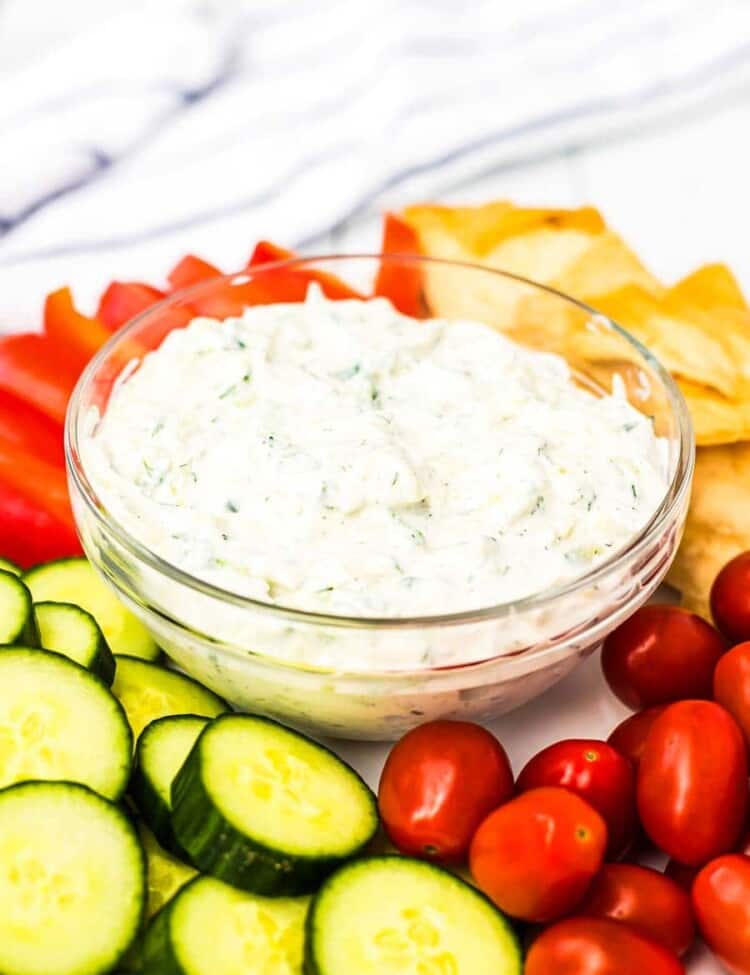 Tzatziki sauce in a glass bowl surrounded by vegetables