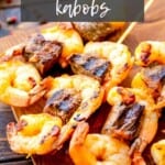 Steak and shrimp kabobs on a wooden cutting board