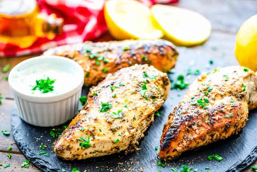 Grilled Greek chicken breasts with sauce on a slate tray.