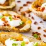 Smoked Potato Skins Pin Image. Complete smoked potato skins garnished with sour cream, chives and bacon on a white cutting board.