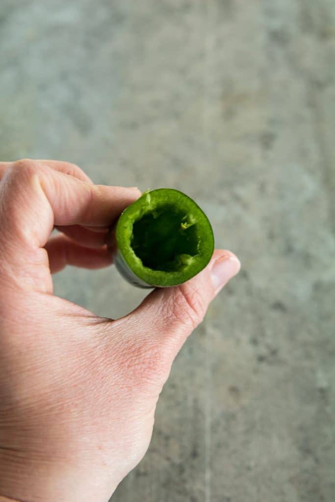 Hand holding cored jalapeno pepper with concrete background behind it
