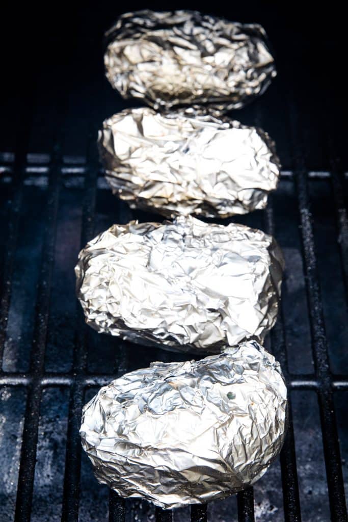 Potatoes wrapped in aluminum foil sitting on the smoker rack.