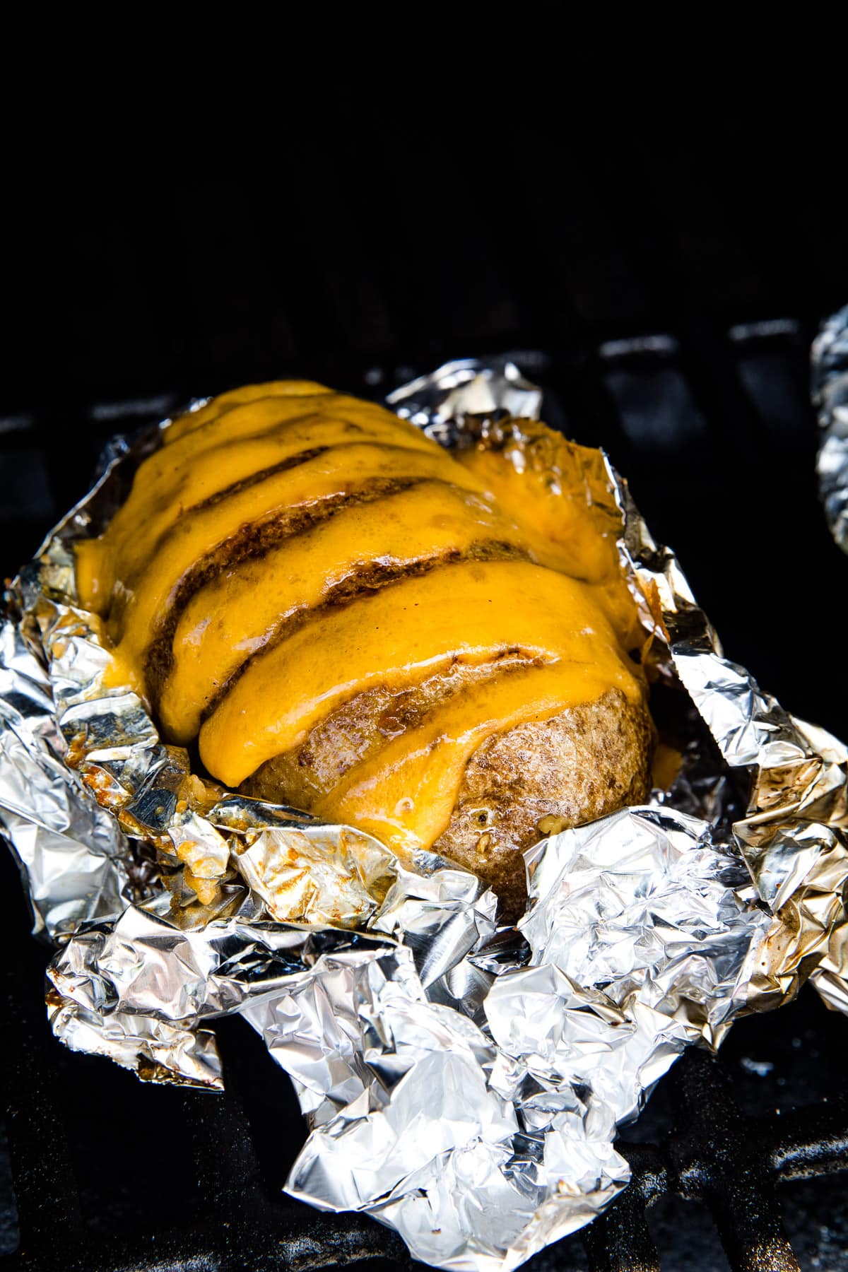 Hasselback Potatoes stuffed with cheese sitting on a piece of aluminum foil on a smoker rack.