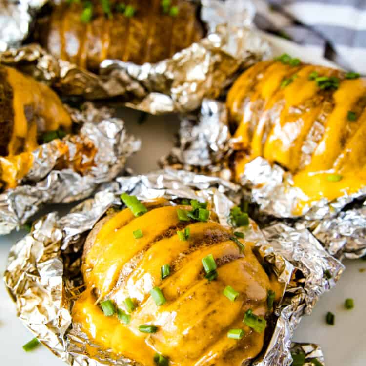 Smoked Hasselback Potatoes stuffed wtih cheese and topped with chopped chives laying on foil that and on a plate.