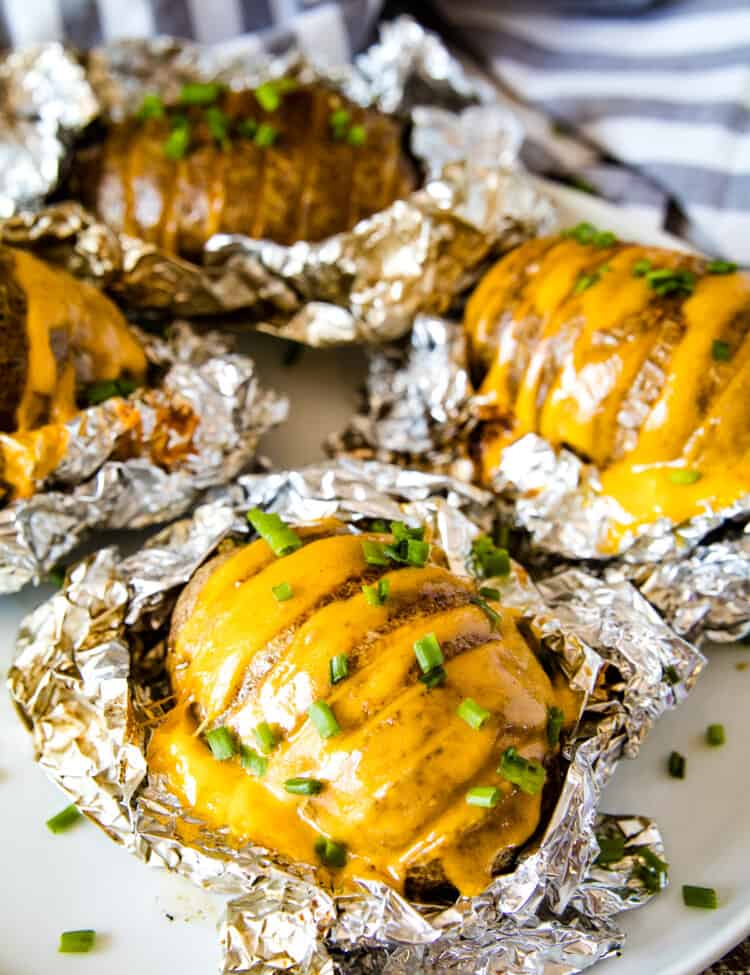 Smoked Hasselback Potatoes stuffed wtih cheese and topped with chopped chives laying on foil that and on a plate.
