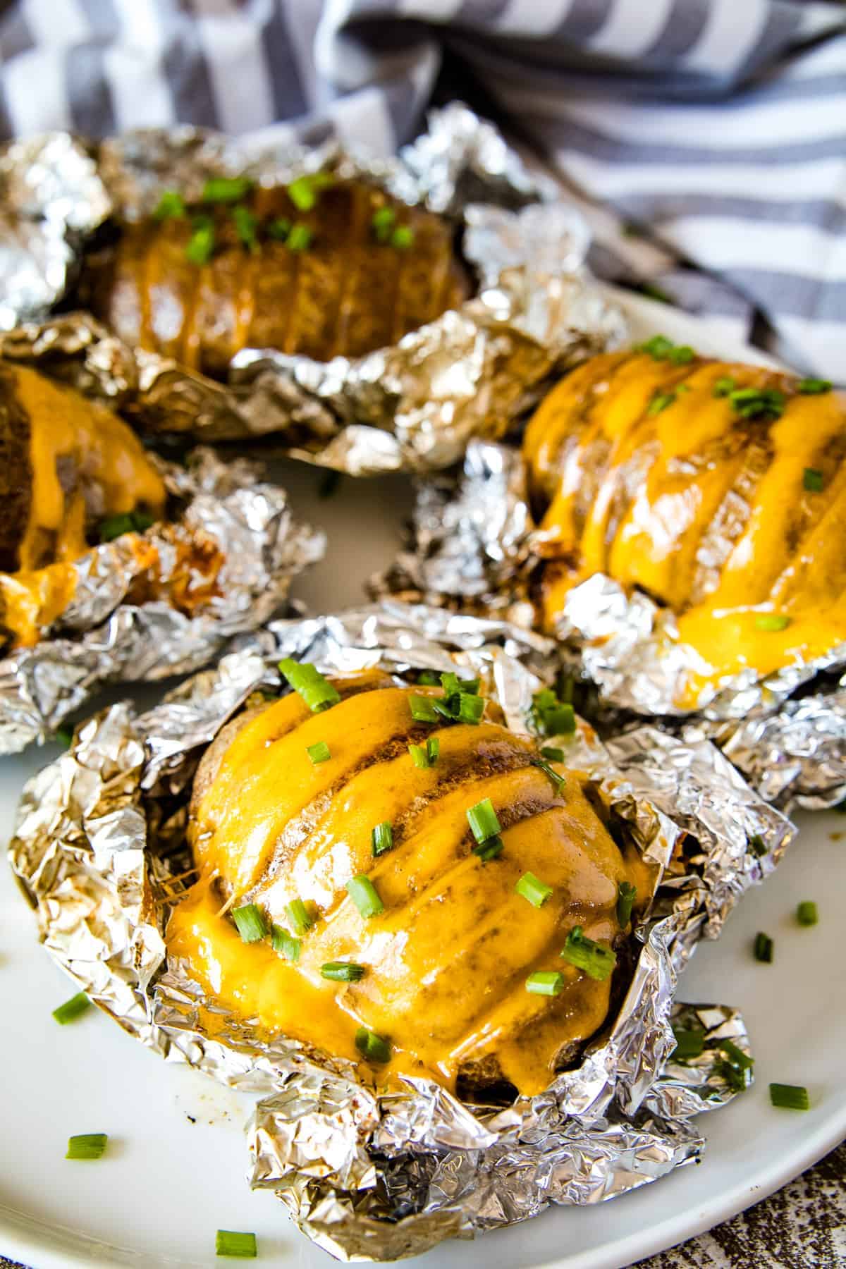 Smoked Hasselback Potatoes stuffed wtih cheese and topped with chopped chives laying on foil that and on a plate.