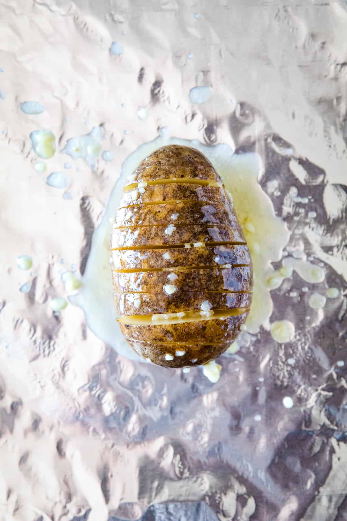 Sliced russet potato that's been brushed with garlic and butter sitting on a piece of aluminum foil.