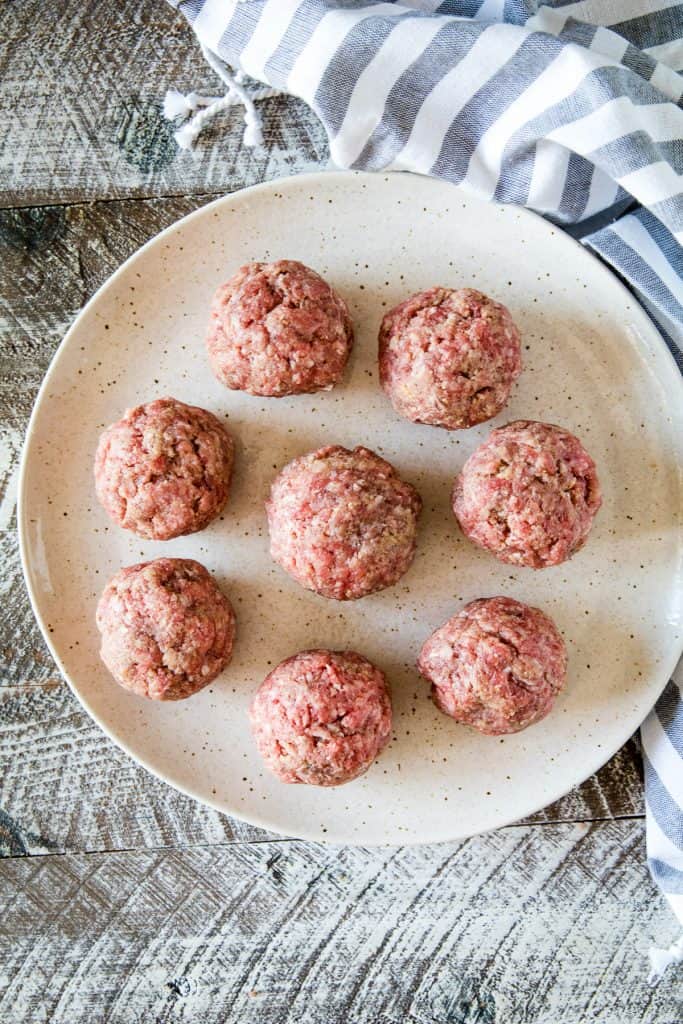 A plate with 8 meatballs that are raw and ready to smoke.