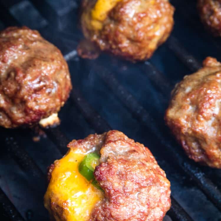 Smoker rack with meatballs on them. Cheese oozing out of them and a jalapeno slice showing.
