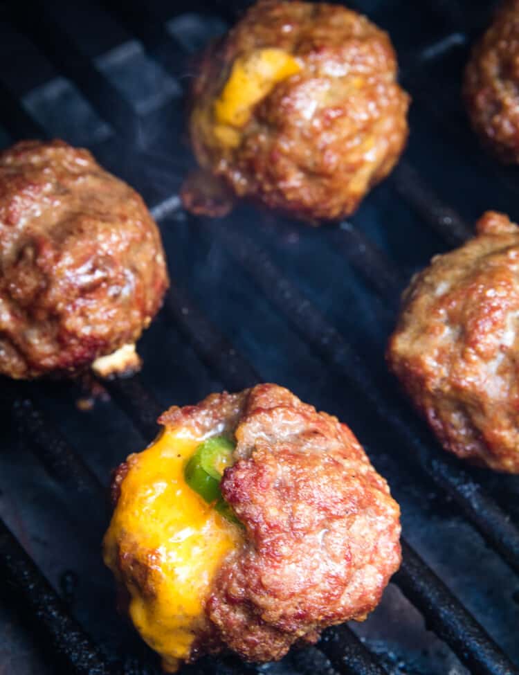 Smoker rack with meatballs on them. Cheese oozing out of them and a jalapeno slice showing.