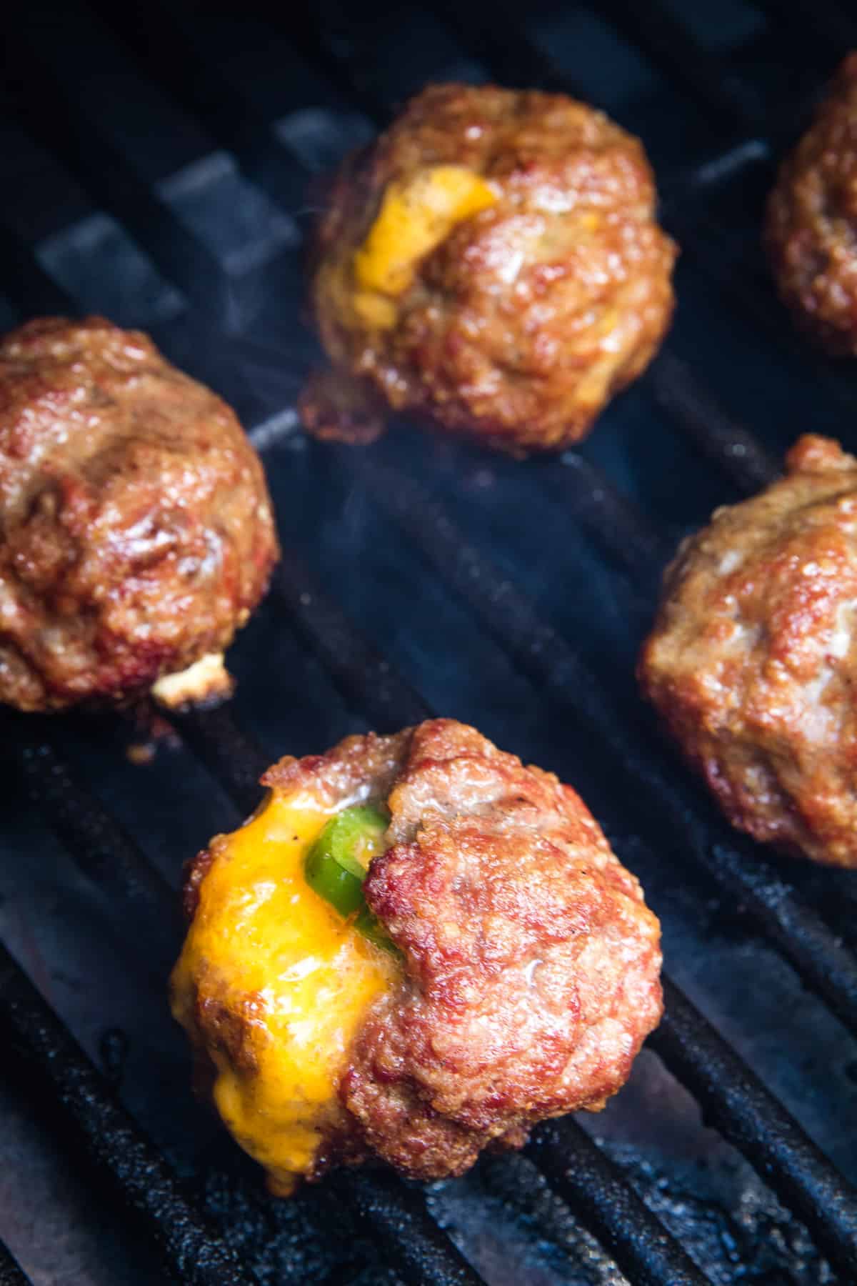 Smoker rack with meatballs on them. Cheese oozing out of them and a jalapeno slice showing.