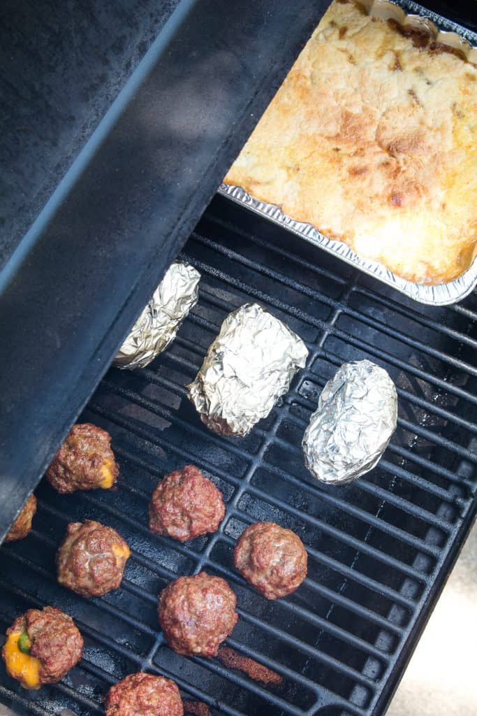 Overhead image of meatballs, foil wrapped potatoes and cake on smoker