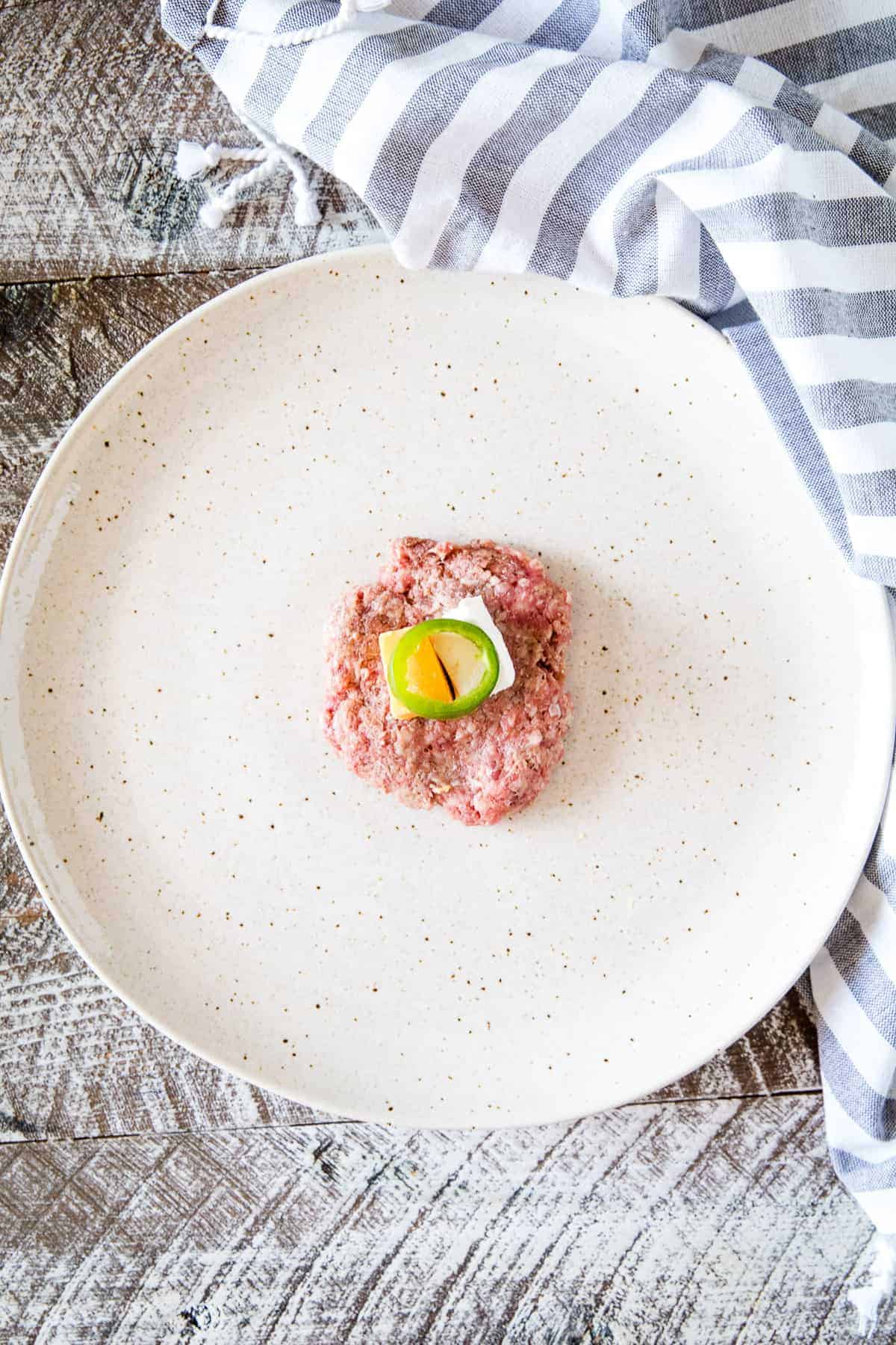 Flattened meatball with a piece of cream cheese, cheese and jalapeno slice in middle