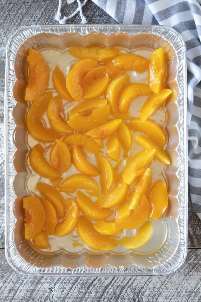 Aluminum foil pan with canned sliced peaches spread evenly over bottom of it. 