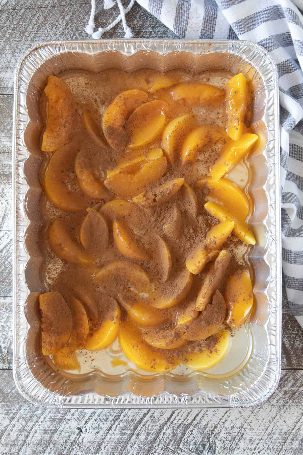 Aluminum foil pan with sliced peaches sprinkled with cinnamon.