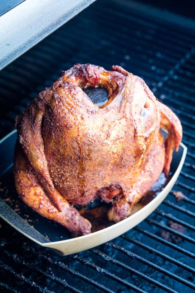 Portrait image of a cooked whole chicken on a beer can holder that's on the smoker.