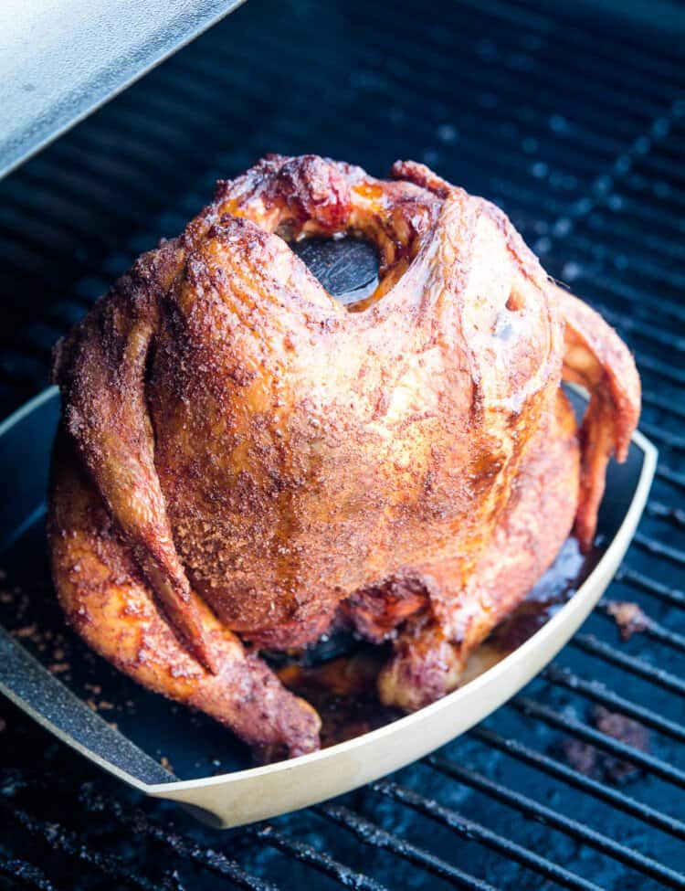 Portrait image of a cooked whole chicken on a beer can holder that's on the smoker.