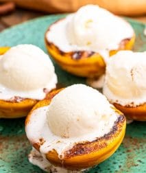 Close up image of four peaches halves that are grilled with a scoop of ice cream on top.