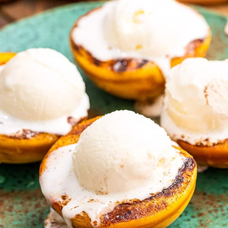 Close up image of four peaches halves that are grilled with a scoop of ice cream on top.