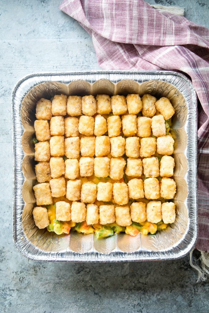 Square foil pan with cheese mixed vegetables in the bottom and topped with frozen tater tots