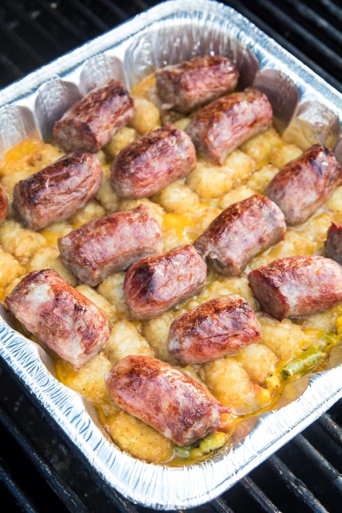 Foil pan with brat tater tot casserole on it on the grill.