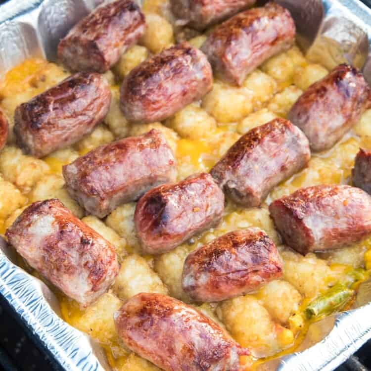 Foil pan with brat tater tot casserole on it on the grill.